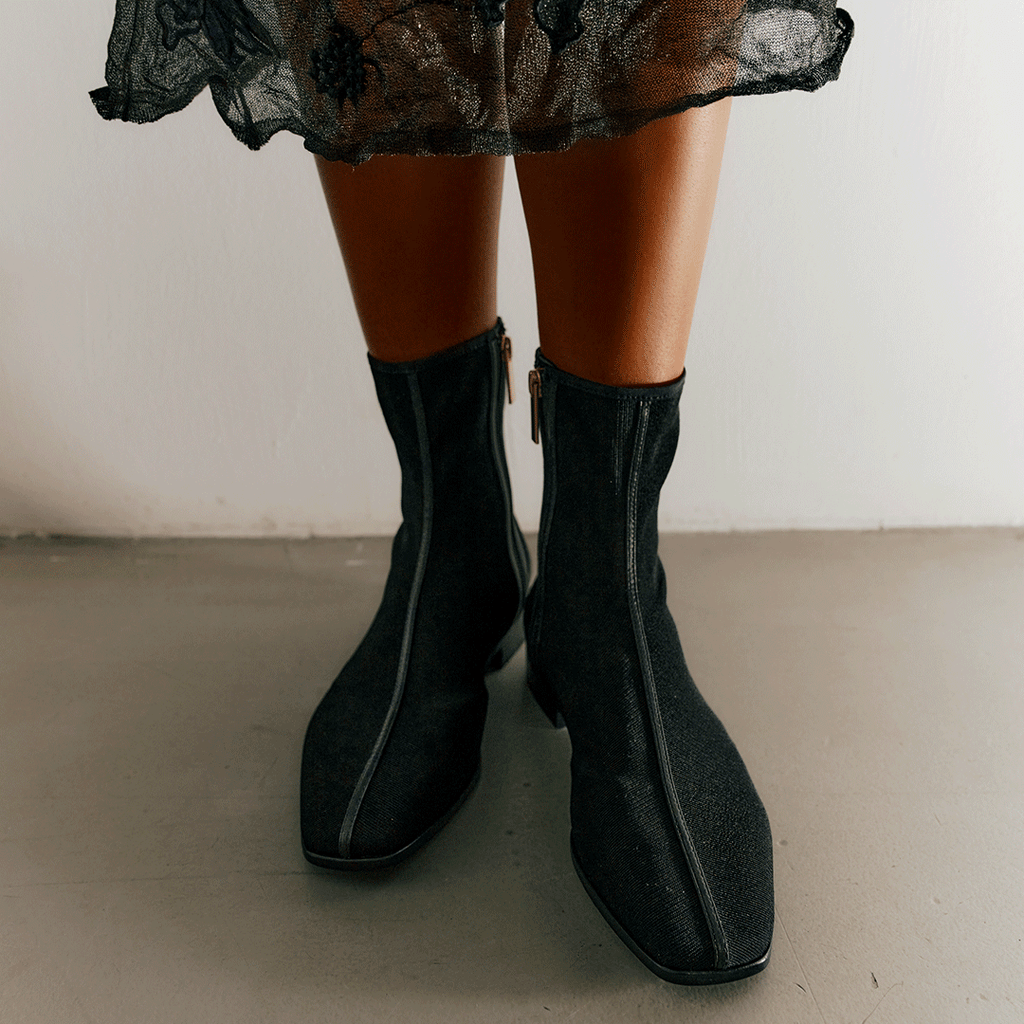 Front-facing shot of model wearing Aliza Black boots, styled with skirt to highlight timeless ankle boot design.