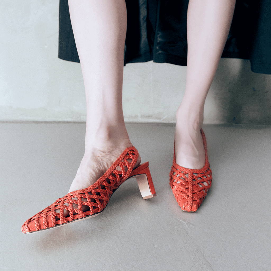 Minimalist style of Cora red braided leather heels worn with a black coat, emphasizing the contrast and elegance.


