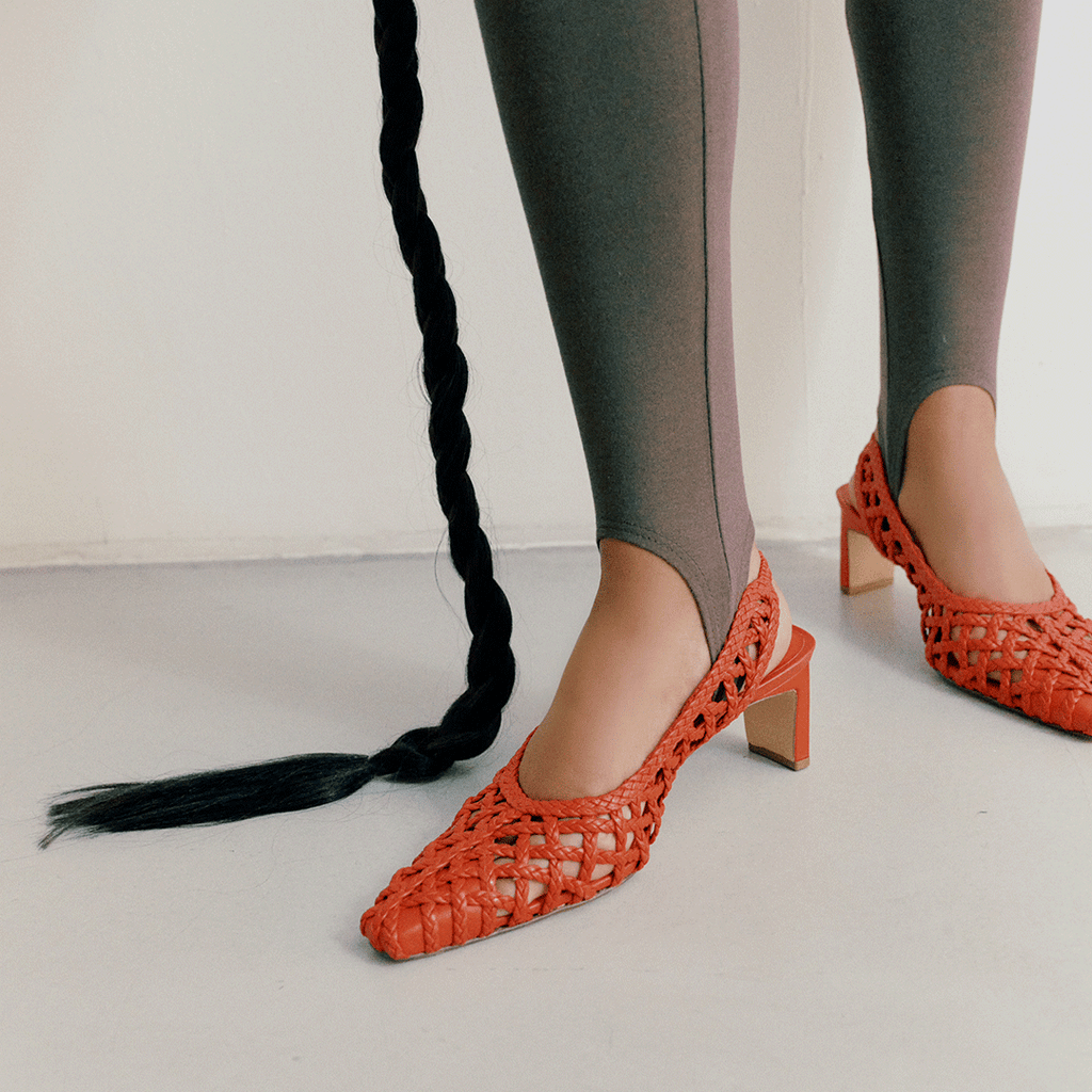 Standing pose wearing Cora red slingbacks, highlighting the woven leather texture and classic heel shape.

