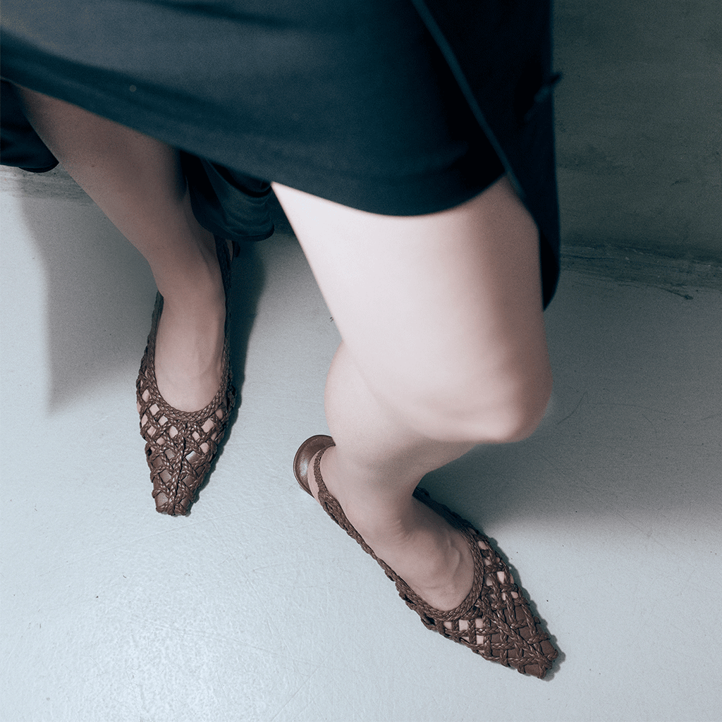 Cora brown braided leather heels styled with a black skirt, showing pointed toe and elegant woven craftsmanship by Daniella Shevel.

