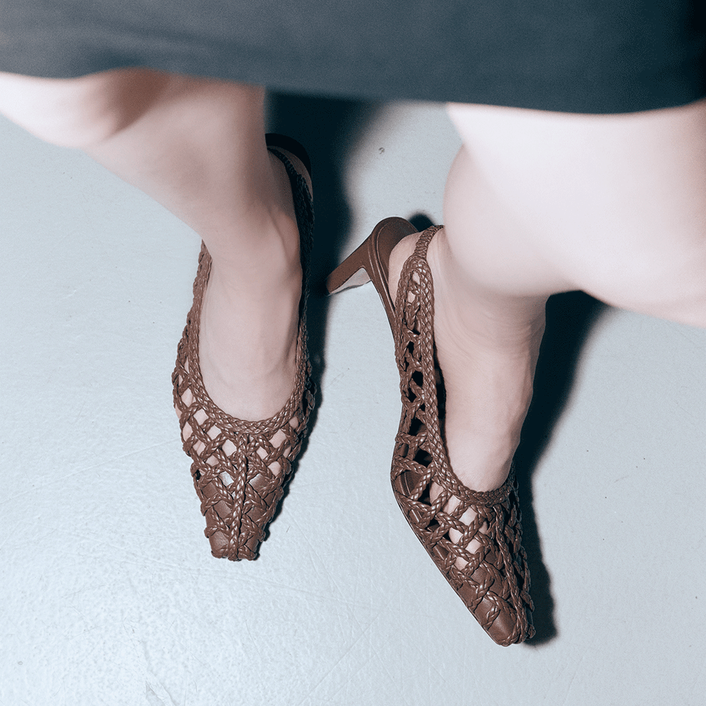 Model stepping forward in Daniella Shevel's brown Cora slingbacks, paired with a black outfit to emphasize the woven leather detail.


