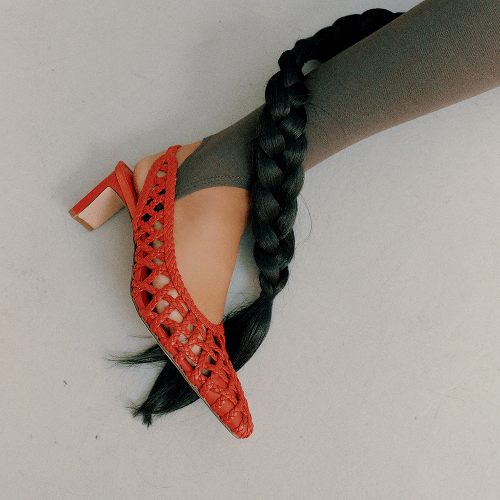 Artistic side angle of the red Cora slingback heel, showcasing the handcrafted braided leather and structured form.

