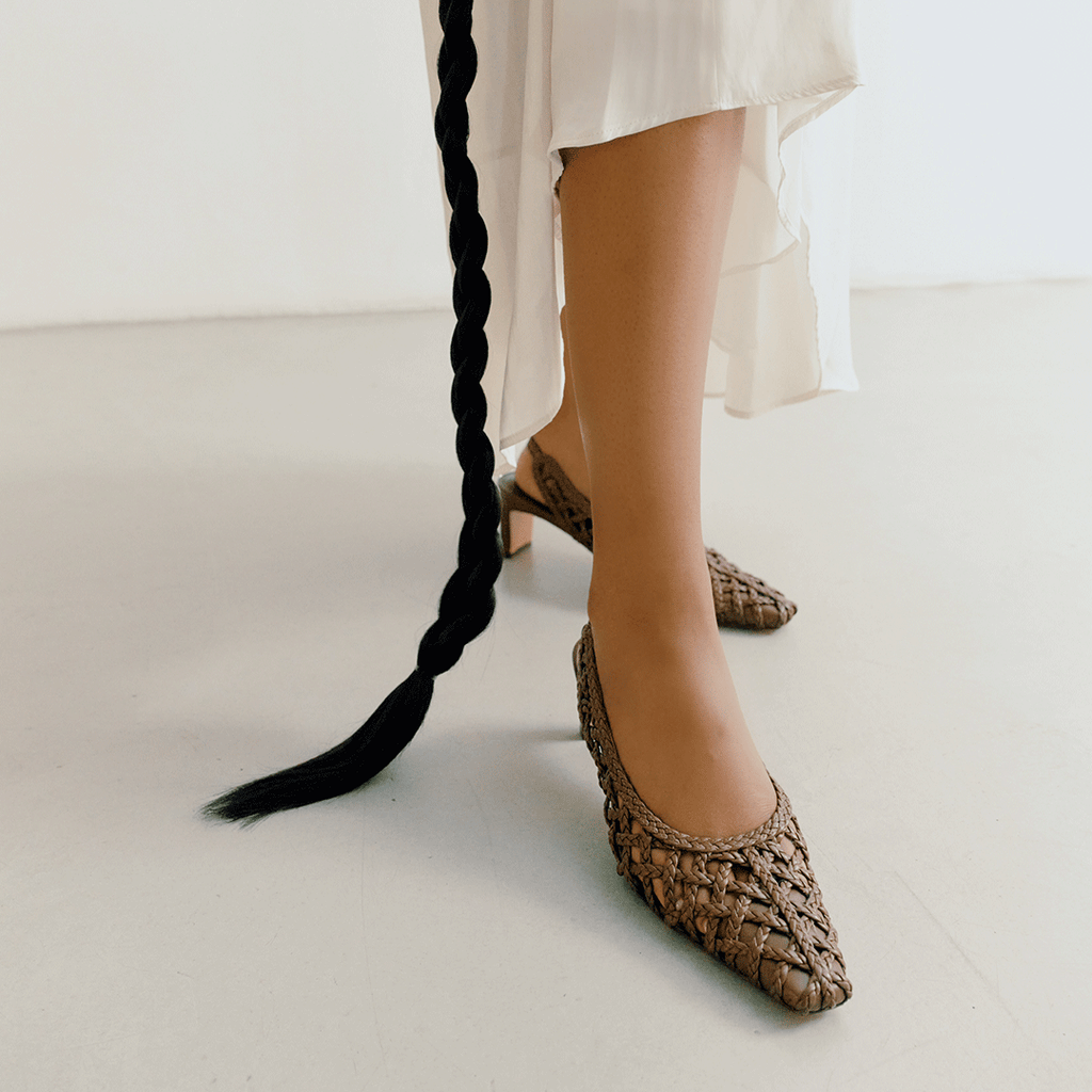 Close-up of Daniella Shevel's Cora braided leather slingback heels in brown worn with a white flowy dress, highlighting pointed toe design.