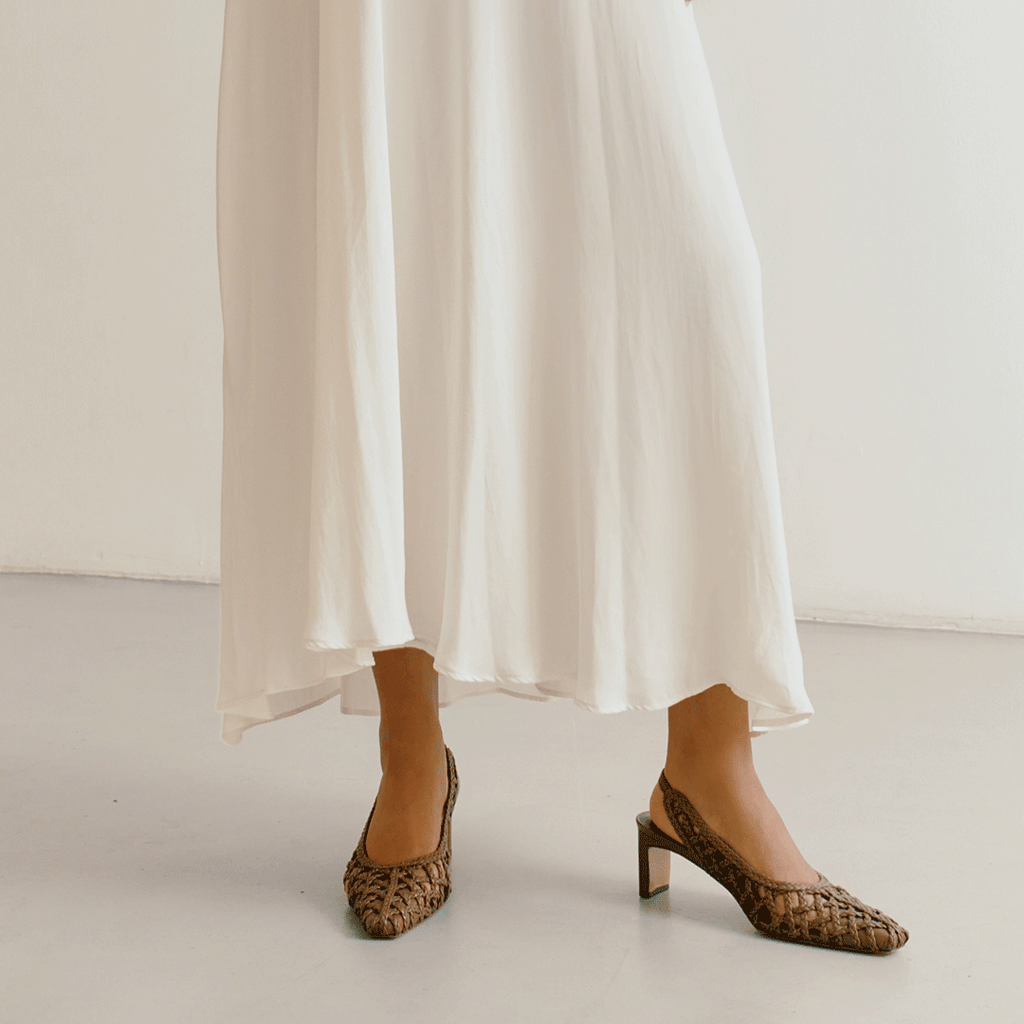 Walking shot highlighting movement and grace of the Cora brown braided slingbacks by Daniella Shevel styled with a light dress.

