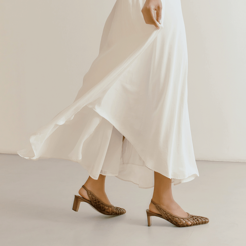Side view of Daniella Shevel's brown Cora heels in motion, paired with a flowing ivory skirt for a soft, feminine look.

