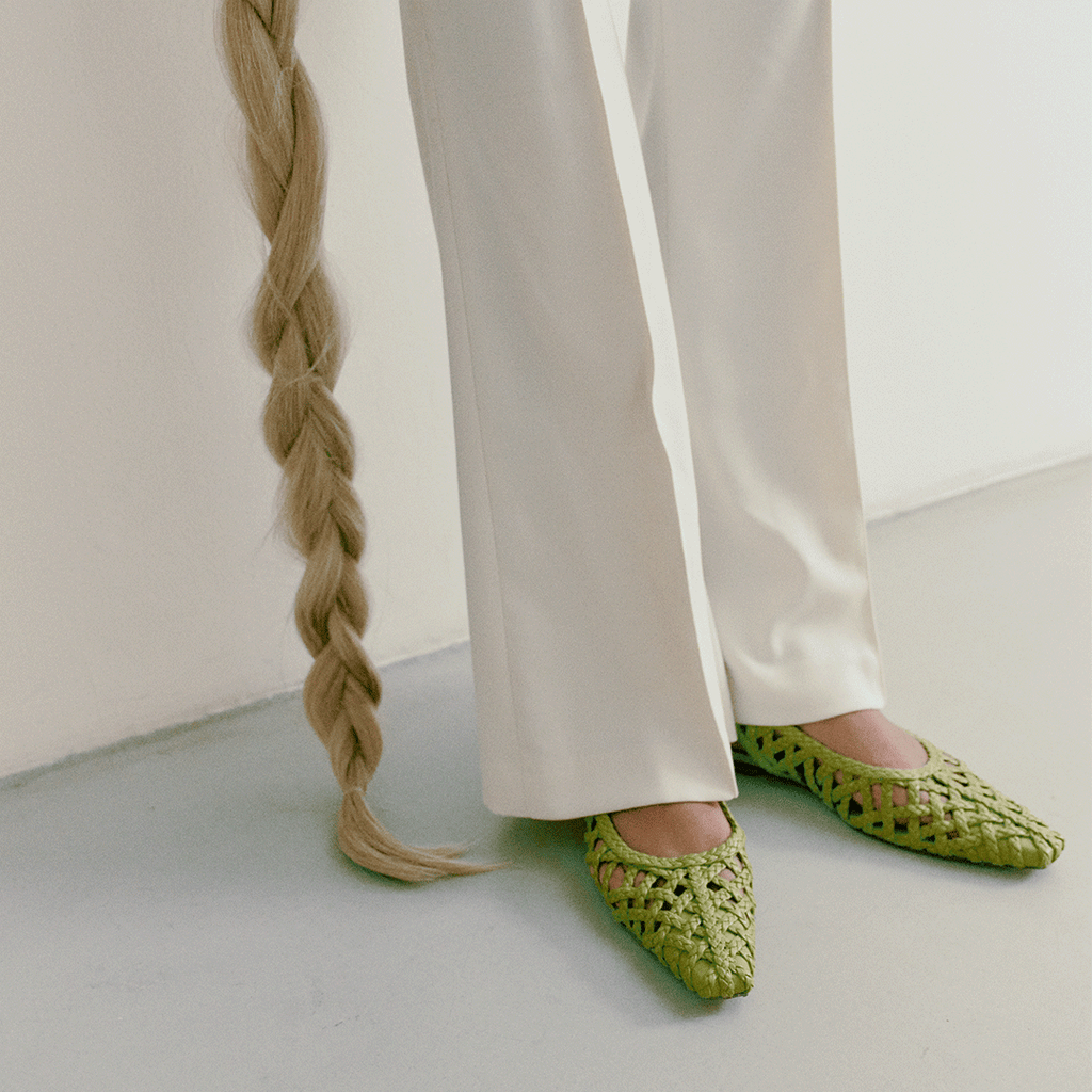 Model wearing Daniella Shevel Halo flats in Wild Moss – styled with ivory trousers and showcasing vibrant green woven leather.