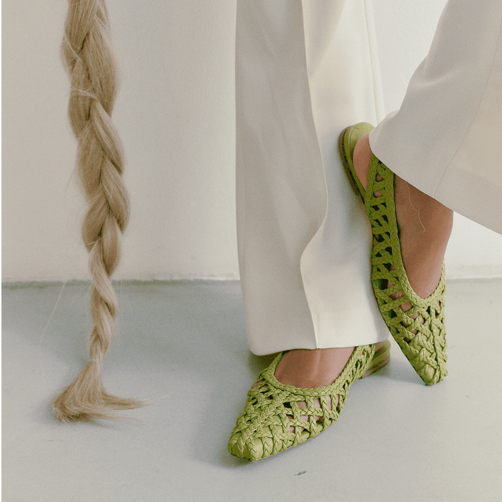 Side step in Halo Wild Moss flats – vibrant color contrasted with off-white trousers and minimalistic backdrop.
