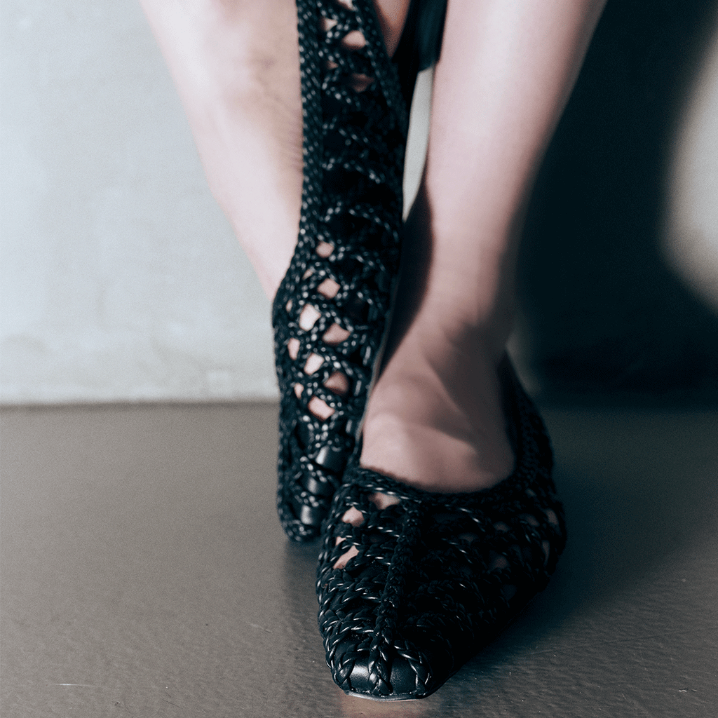 Side view of Daniella Shevel Halo Black flats on model stepping into frame – highlighting handcrafted braid detail and sleek fit.