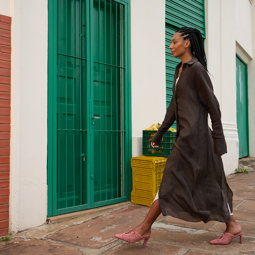 Walking across cobblestone street in Daniella Shevel Bruna raffia sandals in Berry Petal, styled with an airy dress for warm-weather city style.