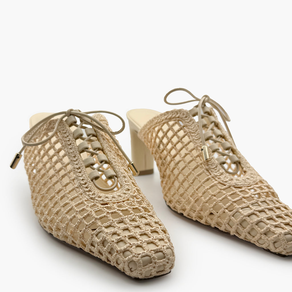 Angled front studio shot of Bruna Mules in Wild Straw – showing handwoven raffia texture, elegant lace-up front, and neutral-toned heel.