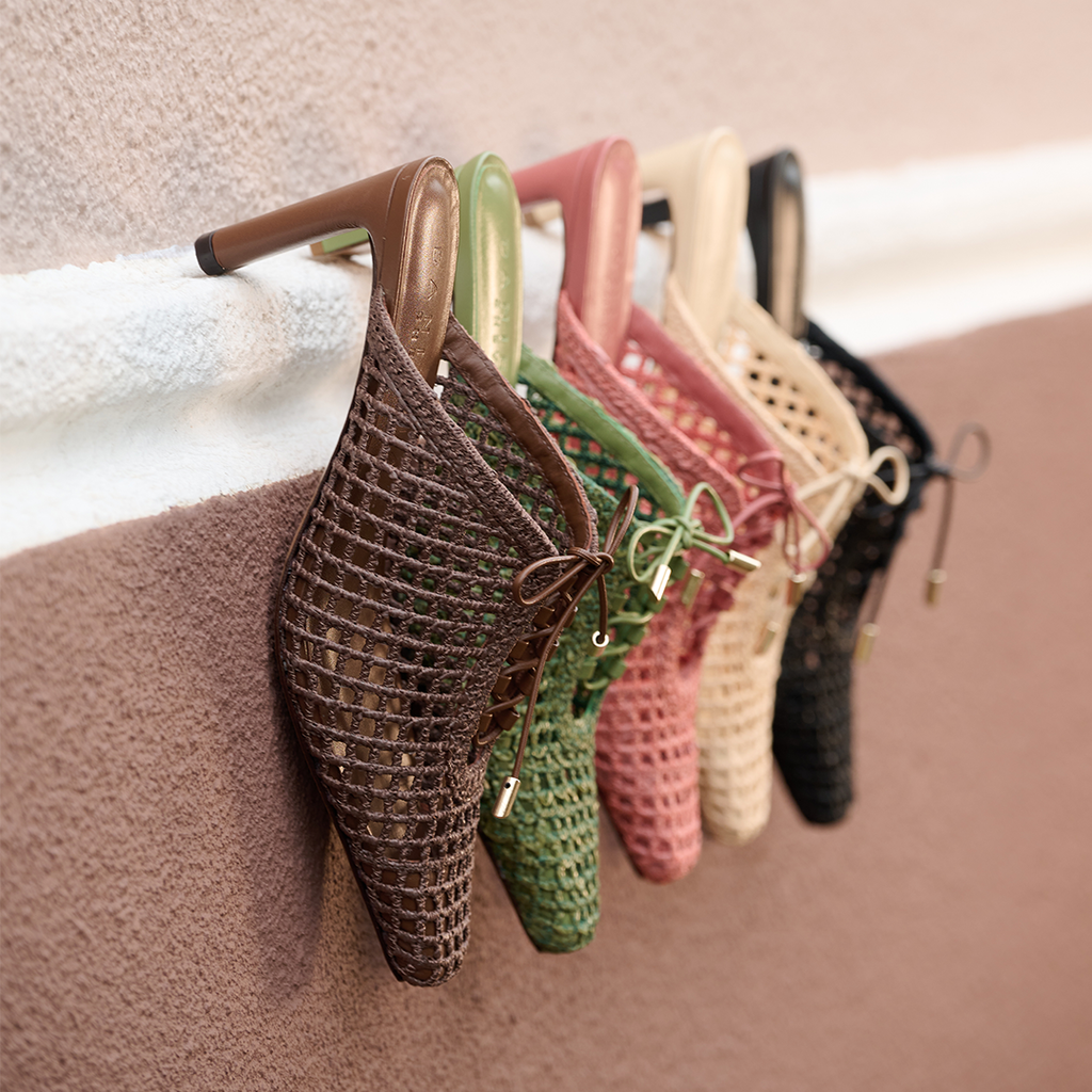 Daniella Shevel Bruna heeled mules in a range of shades including Berry Petal, brown, green, and cream, displayed against a wall to show color variety.