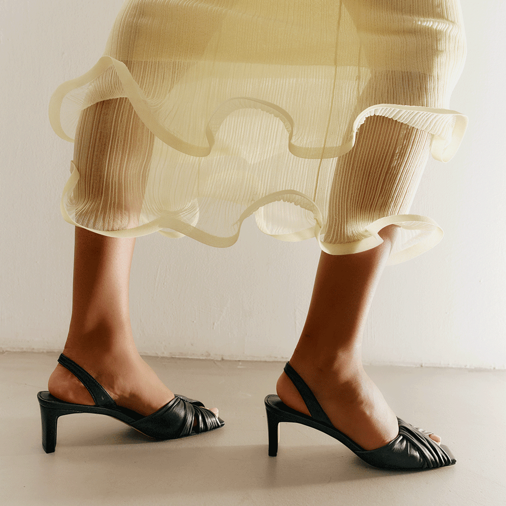 Close-up of Riley black sandals styled with a chic skirt look.