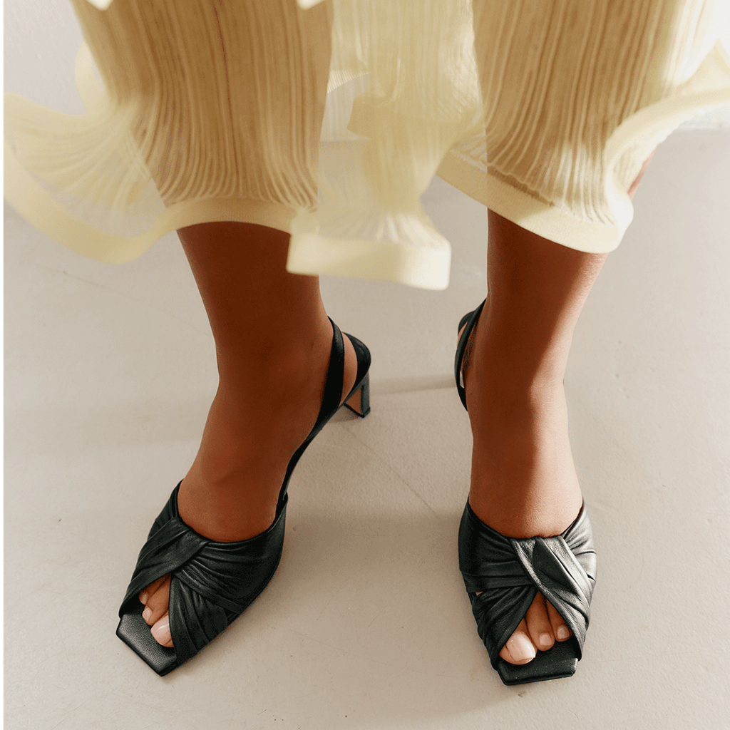 Seated model styling Riley black sandals with minimal outfit.