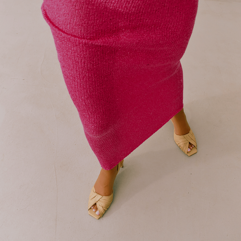 Seated model in pink styling Riley soft oat sandals with minimal backdrop.