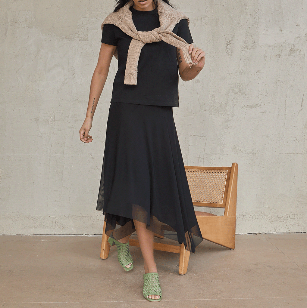 Full-body shot of a woman in a cropped Tshitt, sweater, and black dress, styling the Daniella Shevel woven mule for a modern look