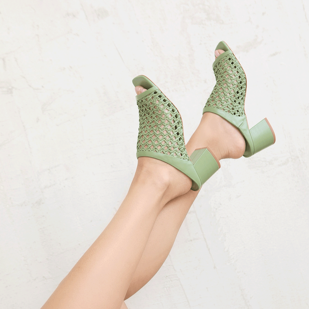 Elevated shot of feet wearing Daniella Shevel green woven mule, showing intricate leather weaving and block heel.