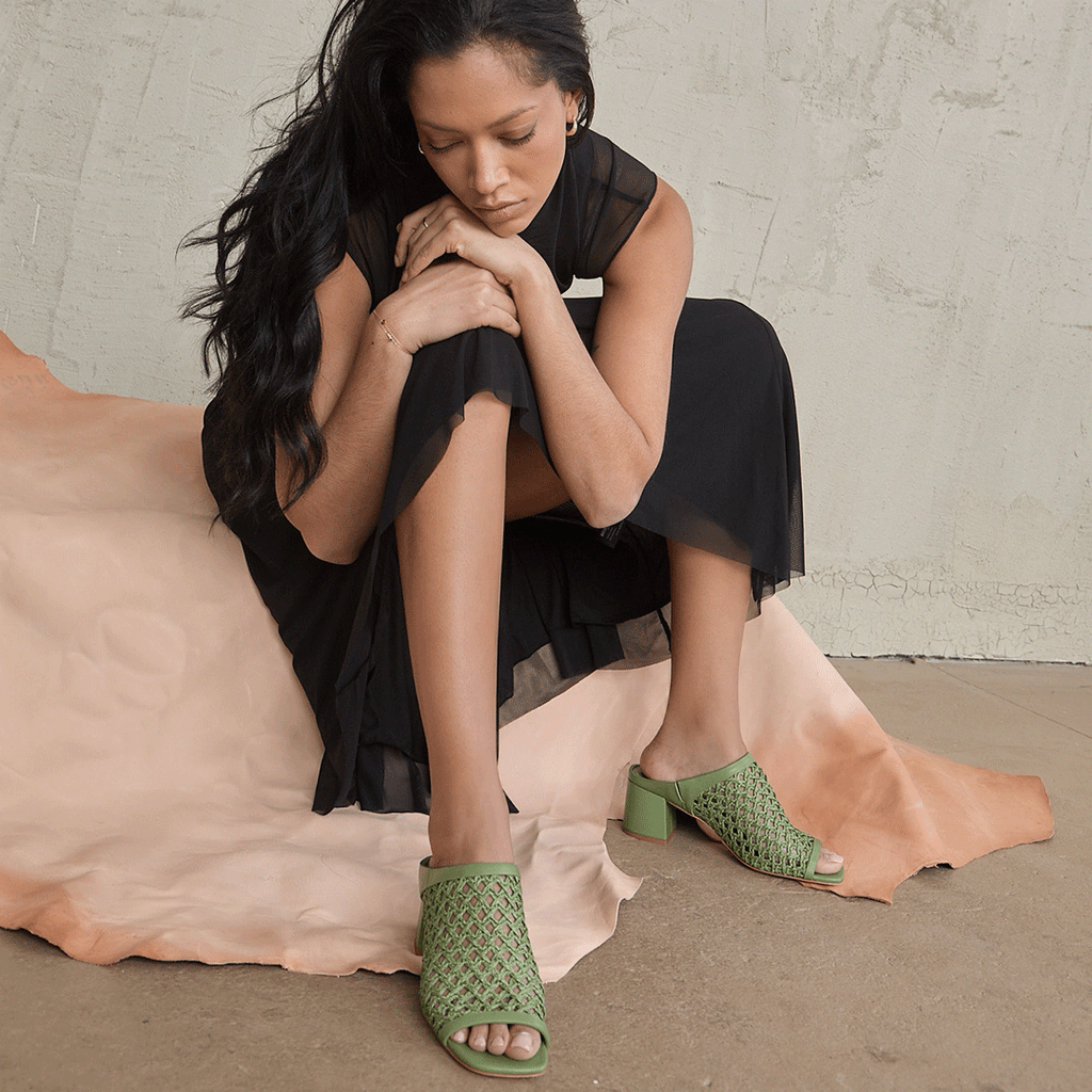 Close-up of a woman sitting with her chin resting on her hand, featuring the Daniella Shevel woven mule in a lifestyle setting.