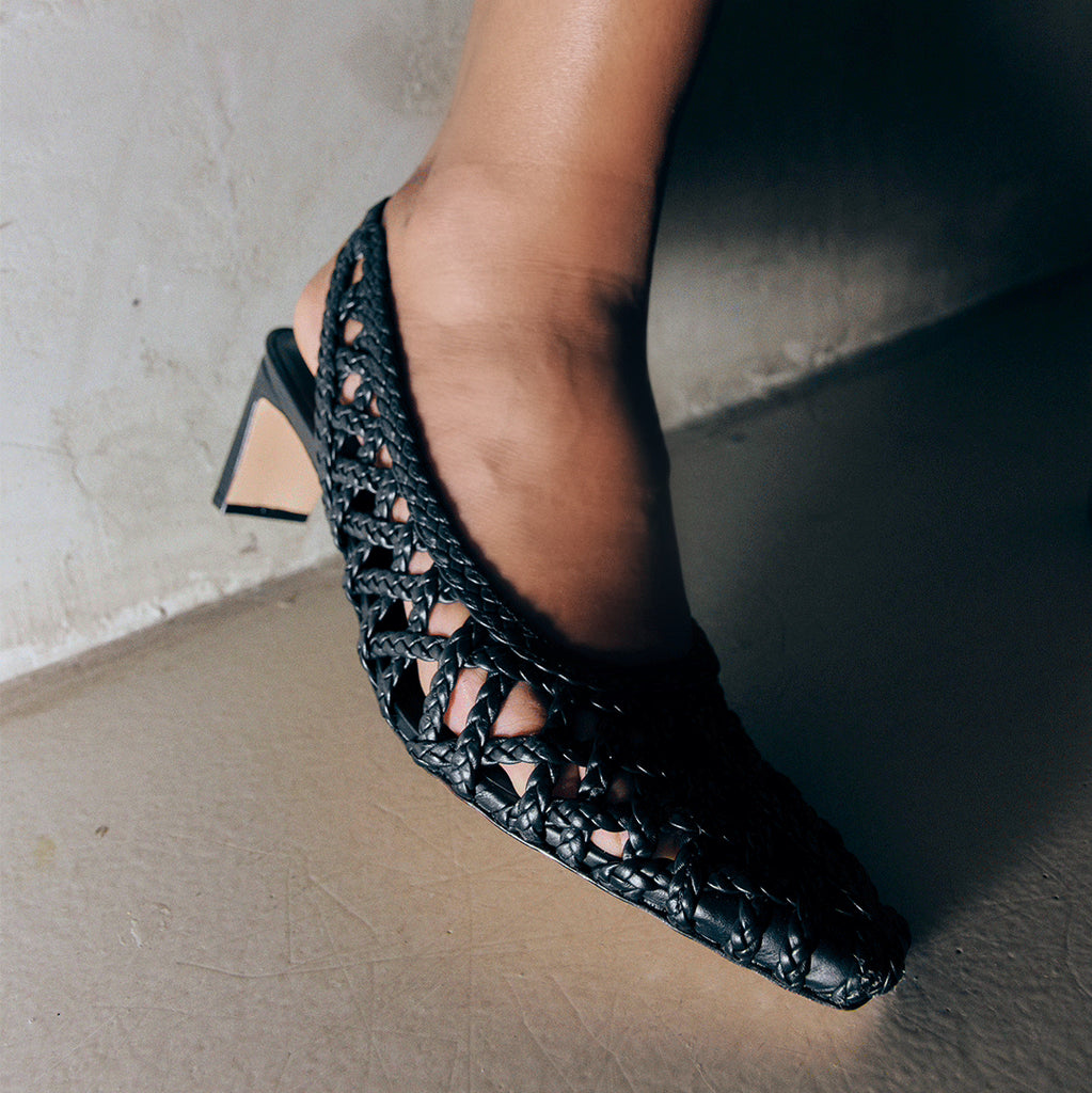 Detailed side view of the Cora slingback in black leather, showcasing the breathable braided pattern.

