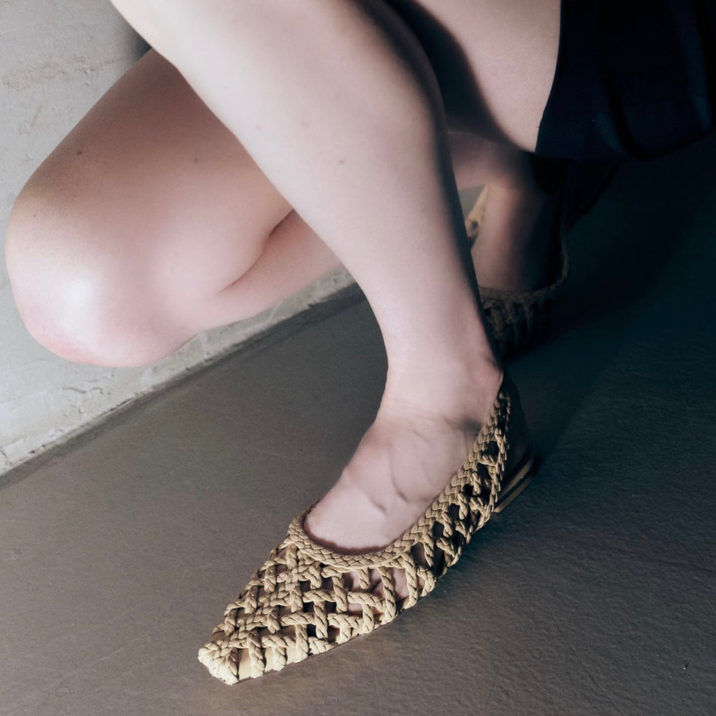 Model crouching in Halo Soft Oat flats – highlighting flexible fit and easy slip-on style in a neutral, minimal palette.